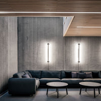 Sleek black sofa with soft gray cushions, set against textured concrete walls and warm wooden accents.