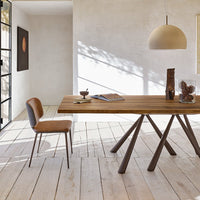 "Natural wood dining table with warm brown tones, paired with a sleek leather chair against light beige walls and flooring."