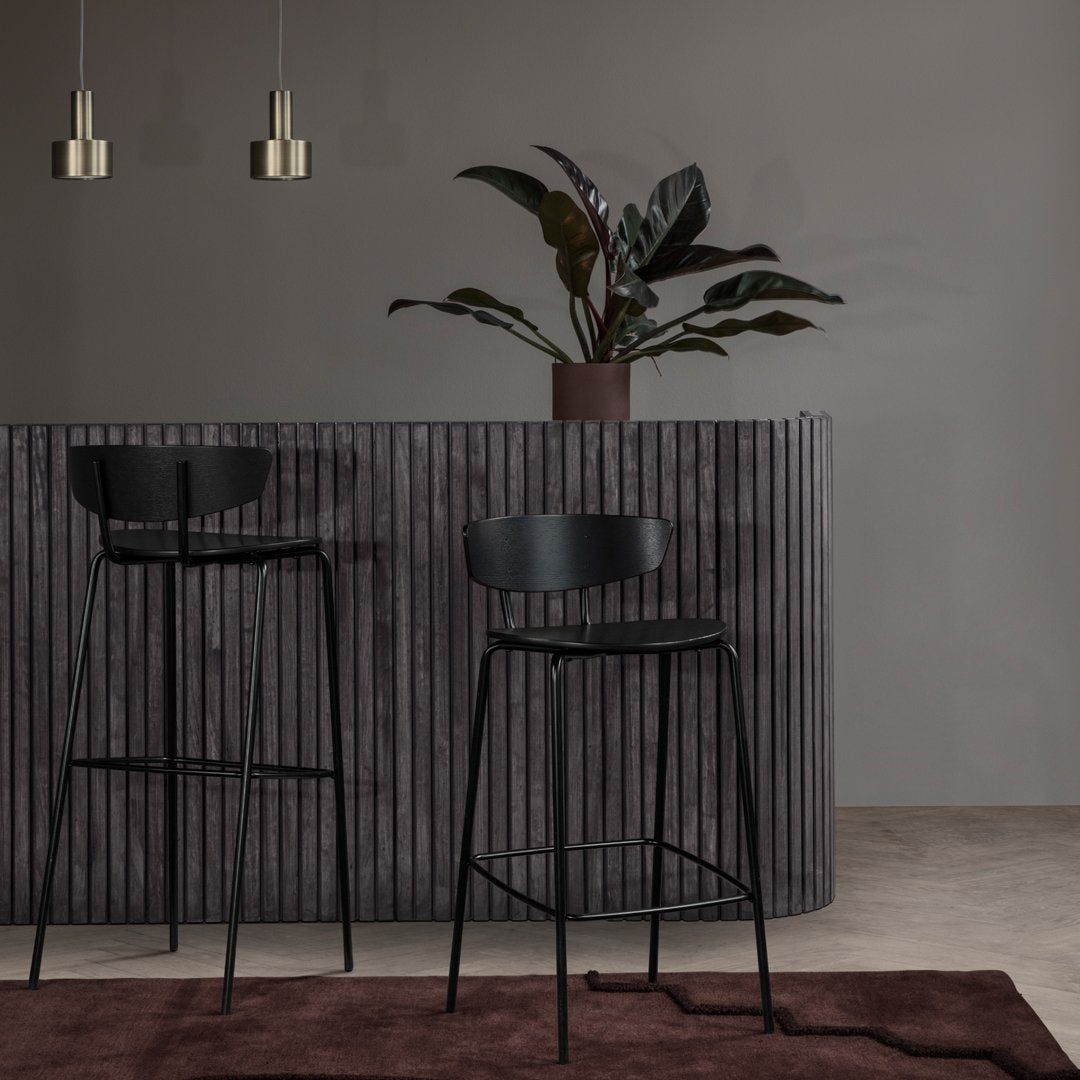 Black bar stools against a textured dark gray bar, with a rich brown rug and green plant accents. Stylish modern decor.