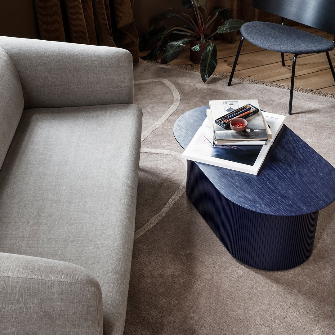Gray sofa with a blue ribbed coffee table on a light beige rug featuring abstract patterns.