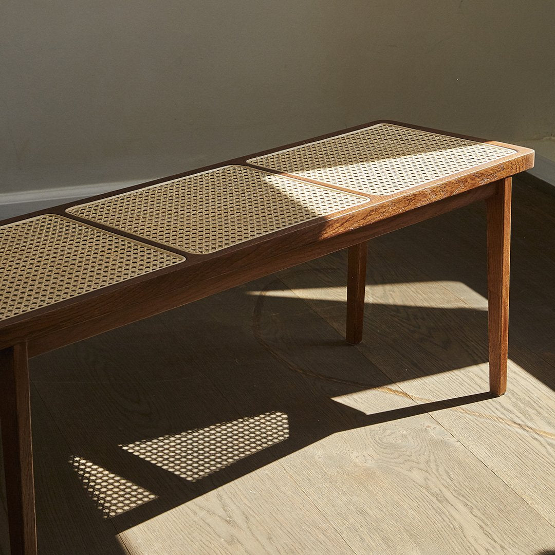 Wooden table with natural cane webbing, featuring a warm brown finish and a light beige woven pattern.
