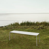 Sleek white outdoor bench with a minimalist design, set against a serene green landscape by the water.