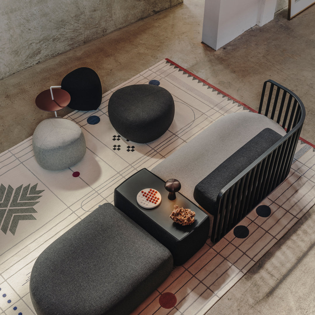 Modern seating in shades of gray, black, and cream, with a geometric patterned rug featuring colorful dots and lines.