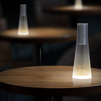 Sleek white lamp design with a transparent base and warm glow, positioned on a wooden table with a rich texture.