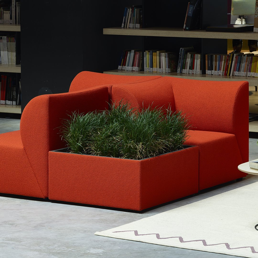 "Vibrant orange sofa with modern design, featuring geometric shapes and a built-in planter with lush greenery."