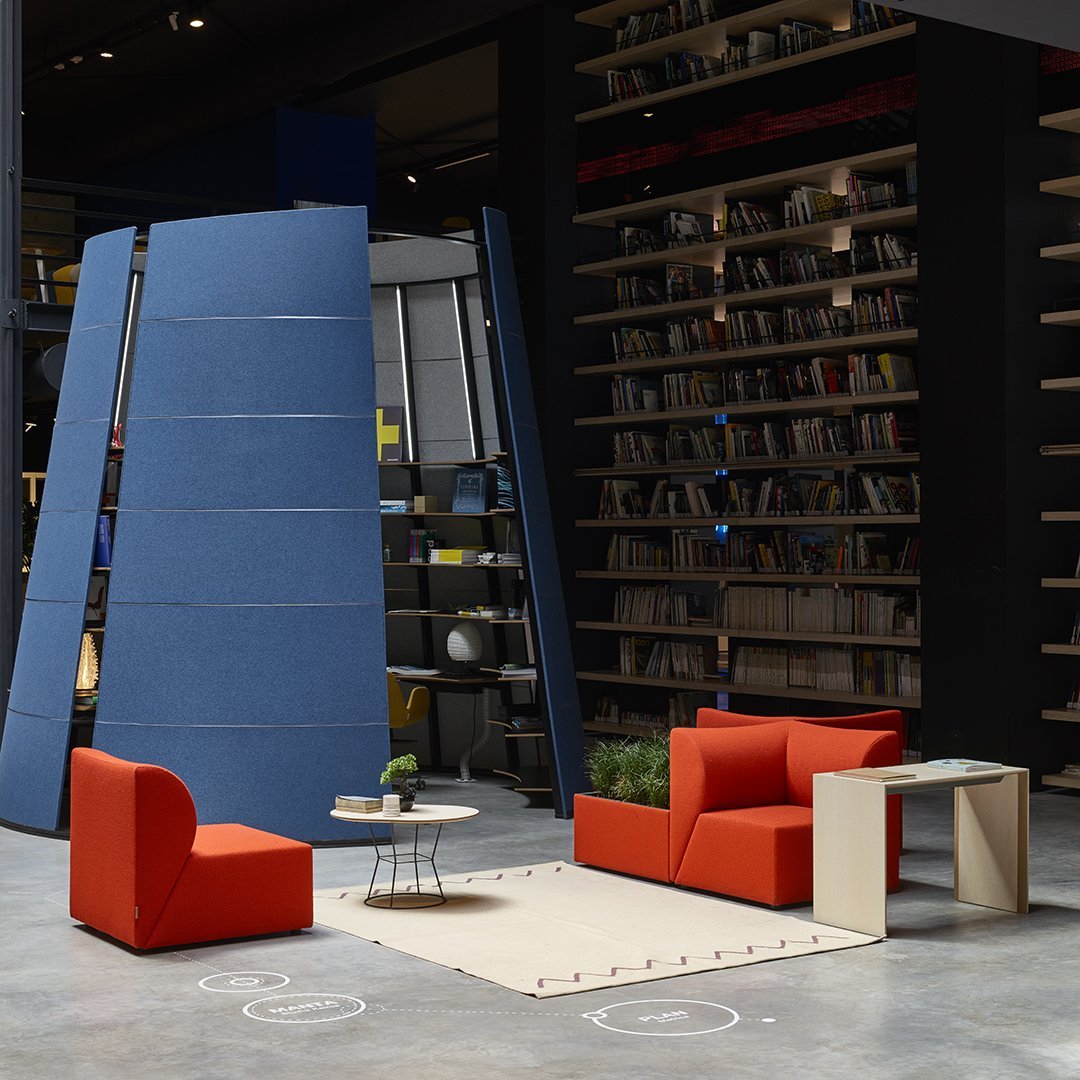 Modern seating in vibrant orange, with a minimalist table, set against a blue backdrop and patterned area rug.