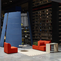 Modern seating in vibrant orange, with a minimalist table, set against a blue backdrop and patterned area rug.
