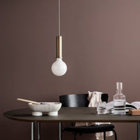 White globe pendant light with a brass accent hanging above a sleek, dark wooden table against a brown backdrop.