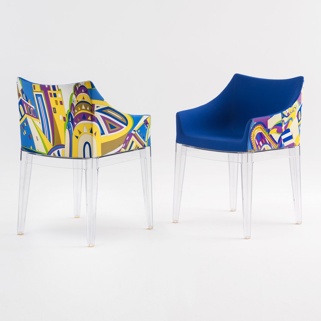 Colorful patterned chair featuring blue upholstery and vibrant abstract designs in yellow, red, and green. Transparent legs.