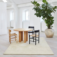 Round oak table with natural wood chairs, black and light wood accents, and a soft beige rug in a bright, minimalist space.