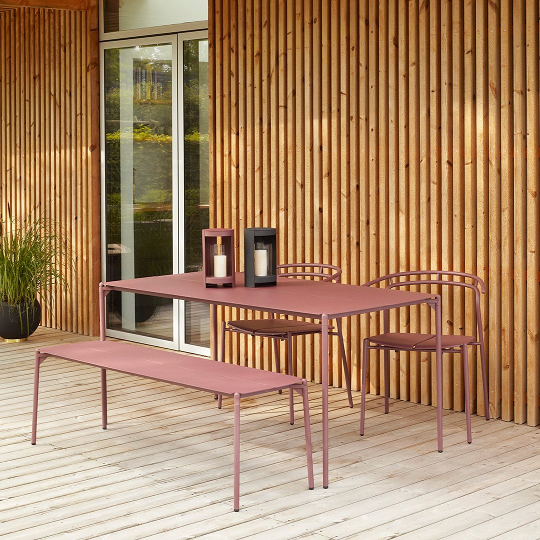 Modern outdoor furniture set in soft pink with sleek lines, paired with black lanterns against a wooden backdrop.