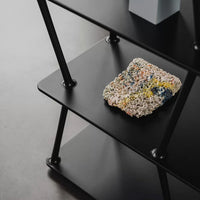 Colorful speckled decorative object in shades of yellow, pink, blue, and cream on a black shelving unit.