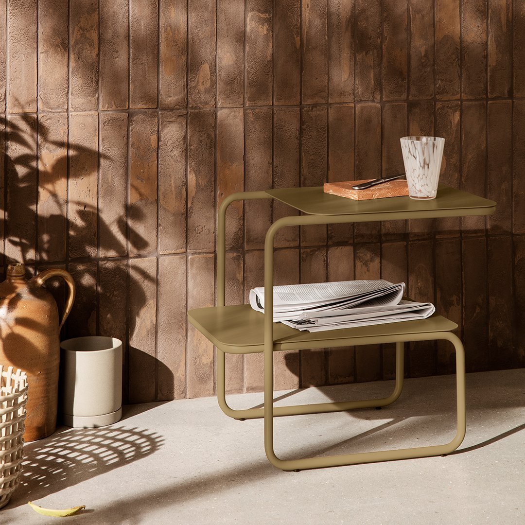 Olive green multi-tiered table with a minimalist design, set against a textured brown wall and natural light shadows.