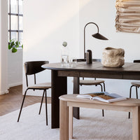 Stylish black dining chairs and a light wood table on a neutral-toned rug in a modern, airy space.