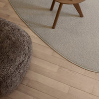 Textured beige area rug with a soft brown pouf and light wooden floor, creating a cozy, neutral palette.