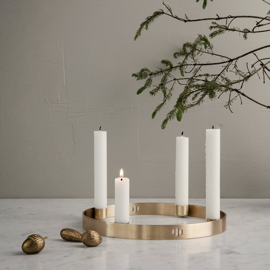 Elegant gold candle holder with four tall white candles on a marble surface, accented by natural greenery.