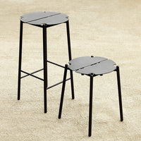 Set of two black metal stools with a minimalist design and circular, slotted tops. Ideal for modern decor.