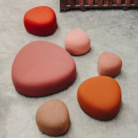 Colorful organic-shaped poufs in shades of red, pink, orange, and peach arranged on a concrete floor.