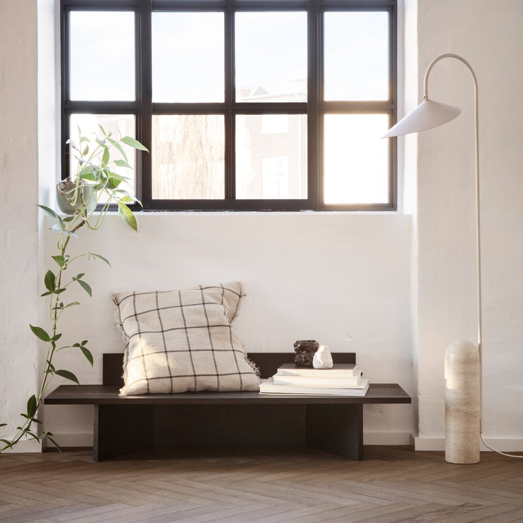 Light wood bench with a black and white checked cushion, surrounded by neutral tones and soft greenery.