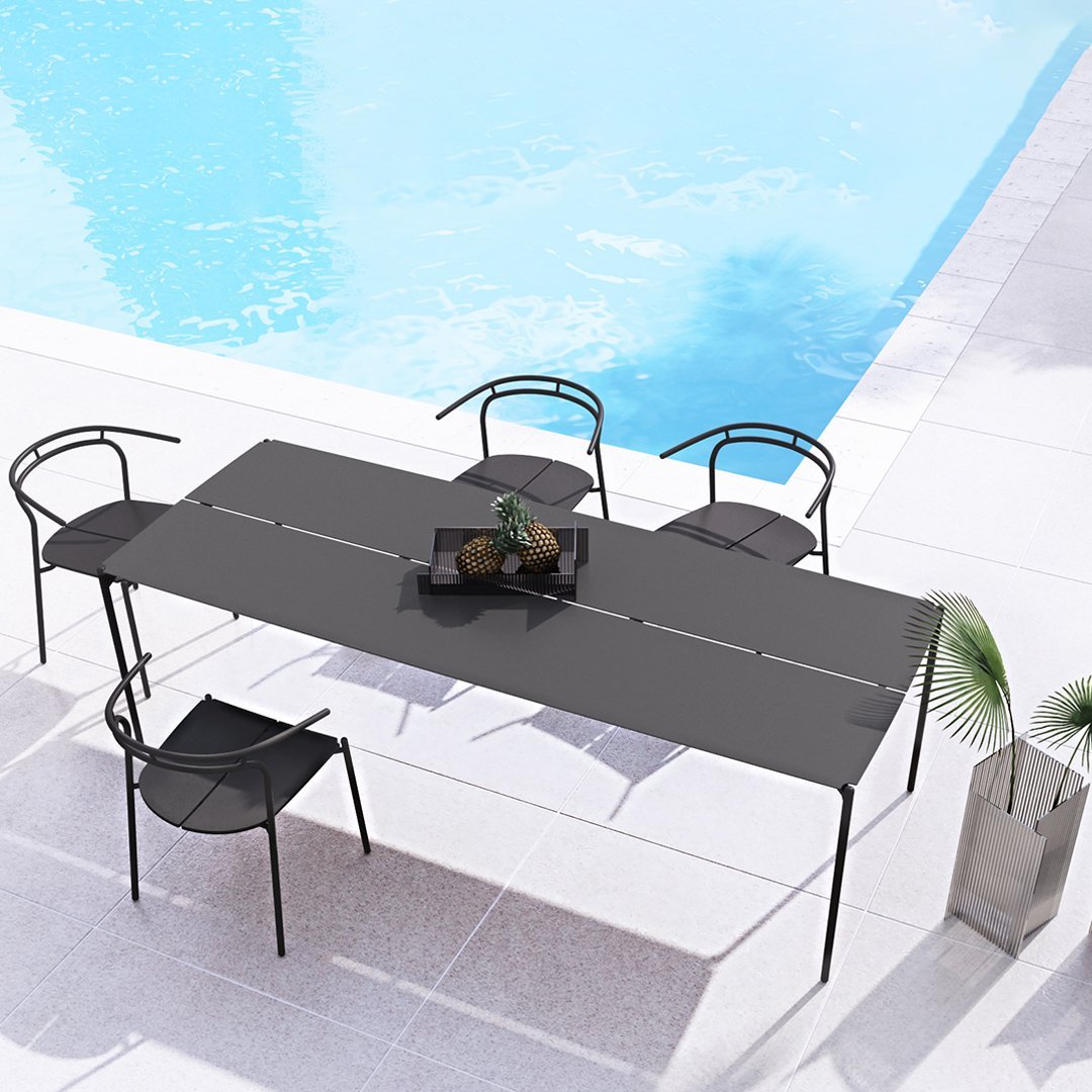 Black rectangular outdoor dining table with sleek, modern design, complemented by black chairs against a tranquil blue pool backdrop.