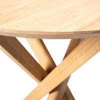 Light oak round tabletop with natural grain, complemented by minimalistic crossed wooden legs in a warm finish.