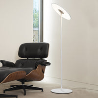 Modern white floor lamp with a sleek circular shade, paired with a black leather chair and wood accents.