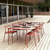 Rustic orange outdoor dining table with round black placemats, surrounded by matching chairs on a wooden deck.