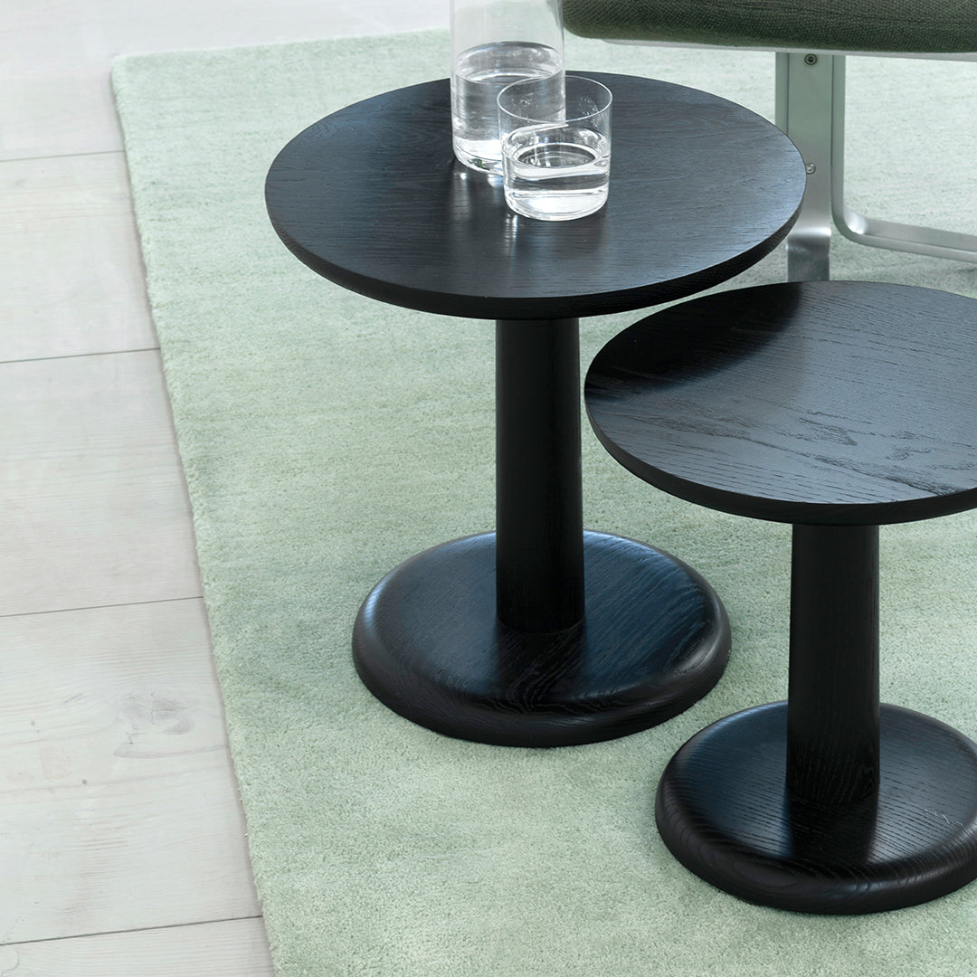 Black round side tables with smooth surfaces, set on a pastel green rug.