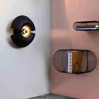 Modern black wall lamp with gold accents against a soft pink wall, featuring sleek geometric patterns.