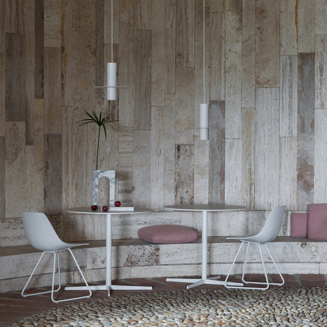 Modern dining set with white chairs and round table against a textured wood panel wall, featuring soft pink cushions.