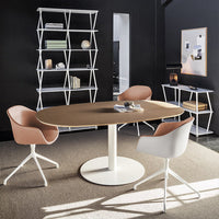 Round wooden table with light brown finish, surrounded by white and soft pink modern chairs in a stylish black room.