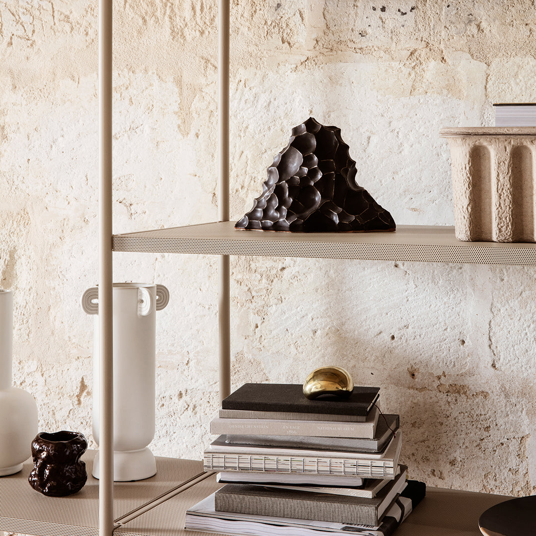 Neutral tones with black, brown, and white accents; textured patterns on vases and books create an elegant display.