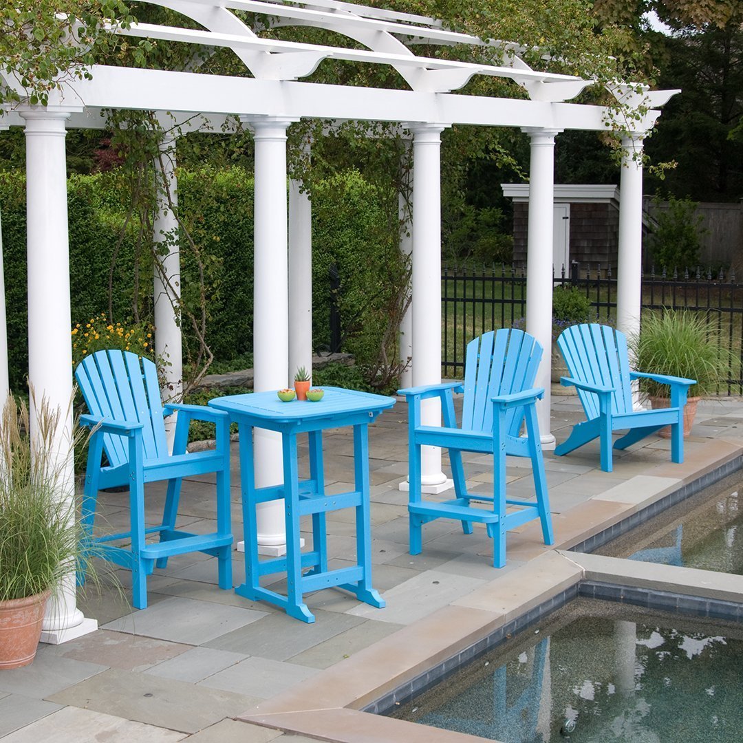 Bright blue Adirondack chairs and matching table beside a pool, complemented by white pergola and lush greenery.