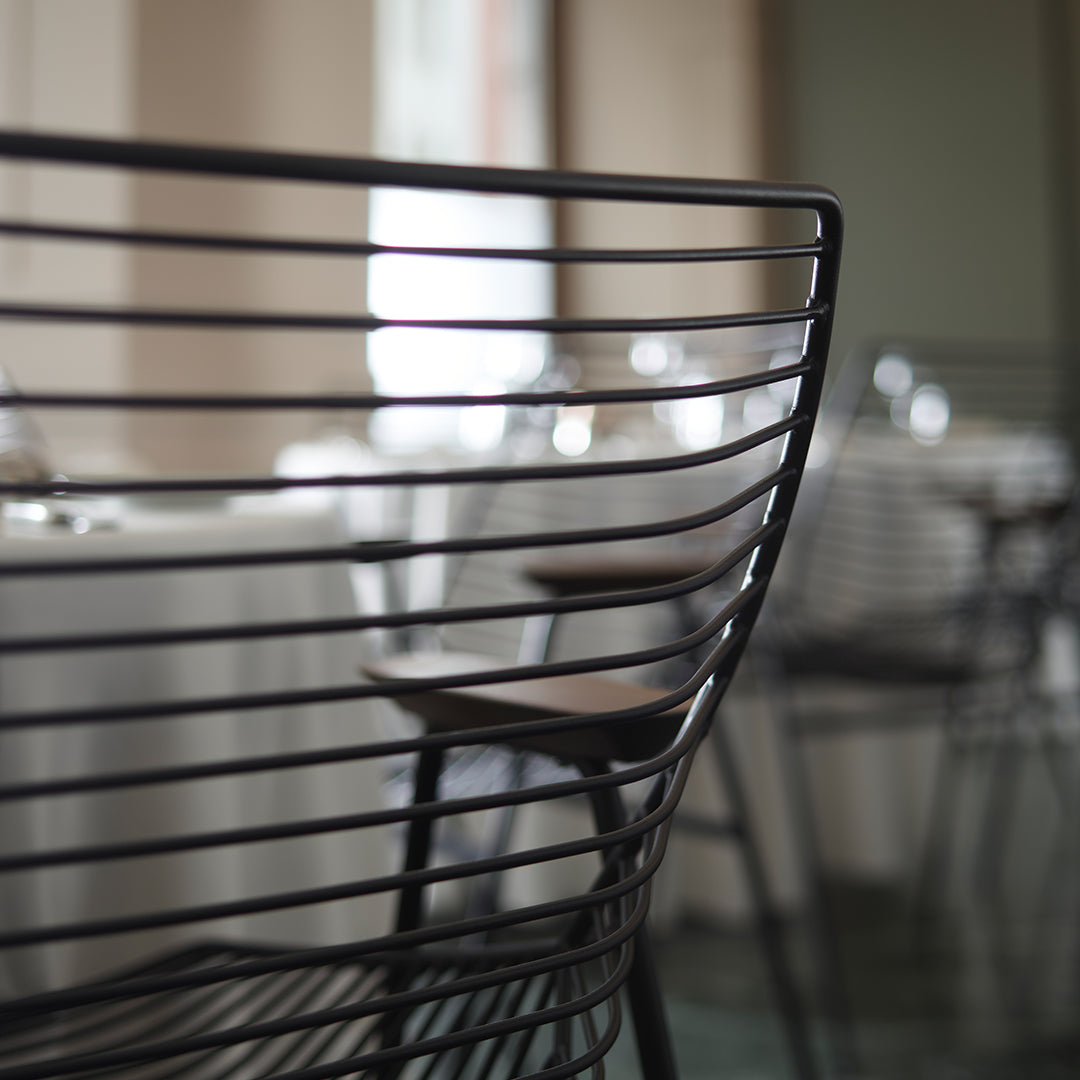Black metal chair with sleek horizontal lines and wooden accents, set in a modern dining environment.