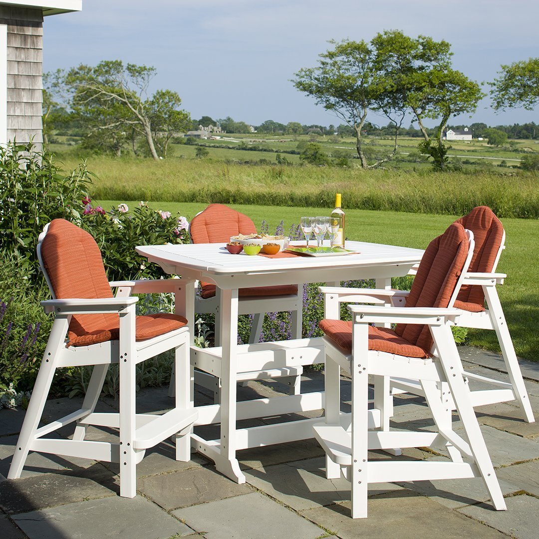 White outdoor dining set with orange cushions, set against a lush green landscape. Ideal for stylish outdoor gatherings.