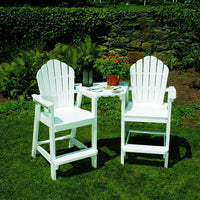 White Adirondack chairs with classic slatted back design, paired with a small table in a lush green garden setting.