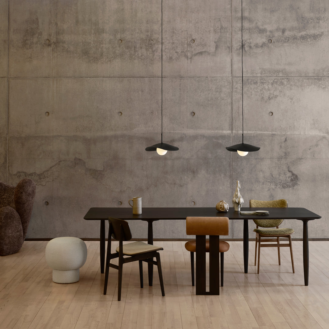Modern dining space with black table, neutral walls, green and tan chairs, and sleek pendant lighting.