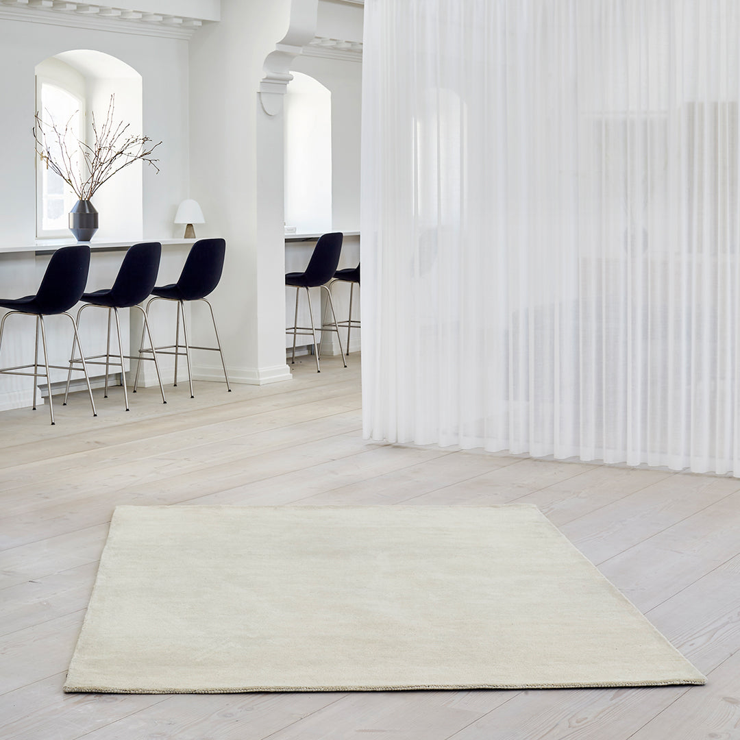 Cream-colored rug with a soft, smooth texture, set against a light wood floor and minimalist backdrop.