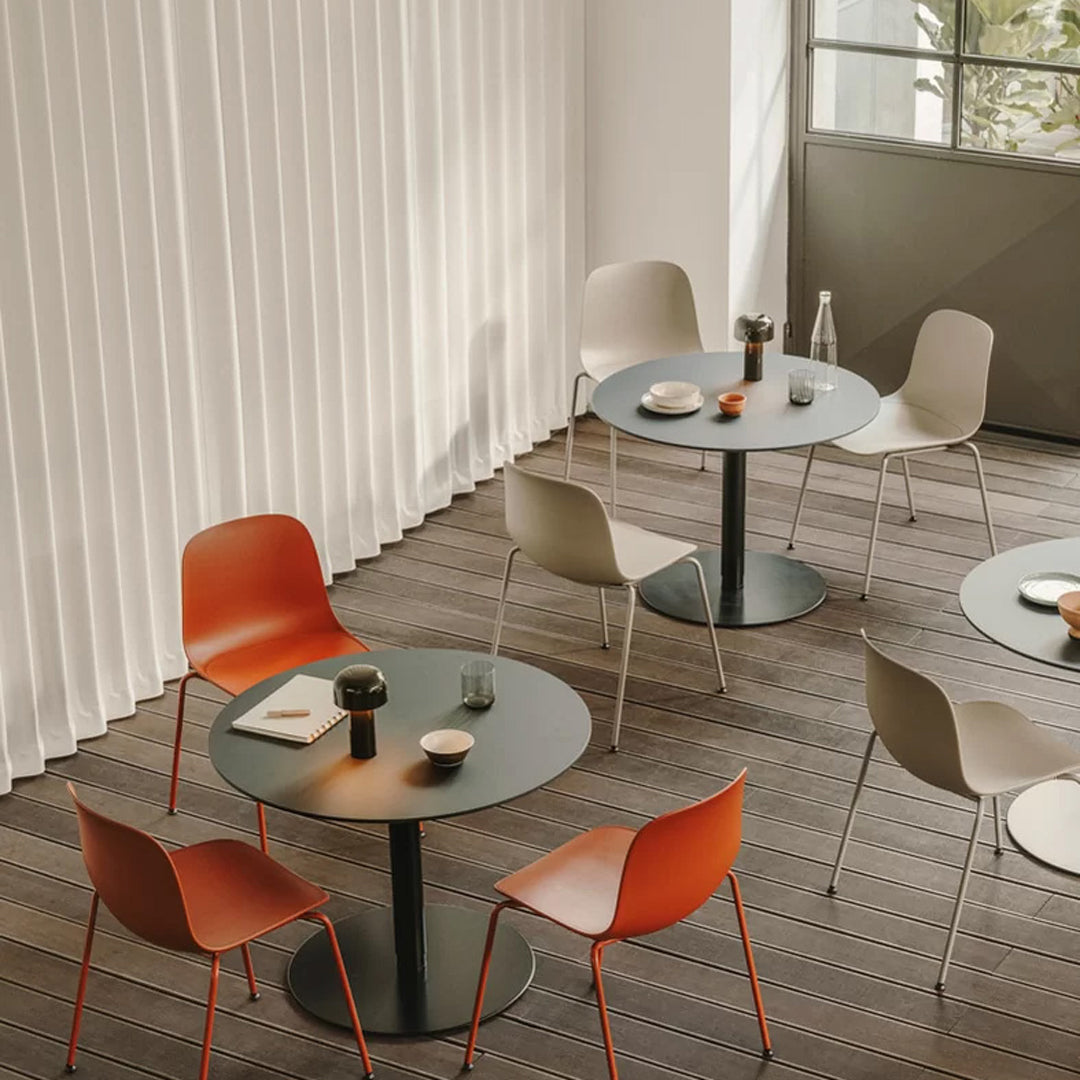 Modern dining set with orange and neutral chairs, featuring round black tables against light wooden flooring.