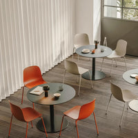 Modern dining set with orange and neutral chairs, featuring round black tables against light wooden flooring.