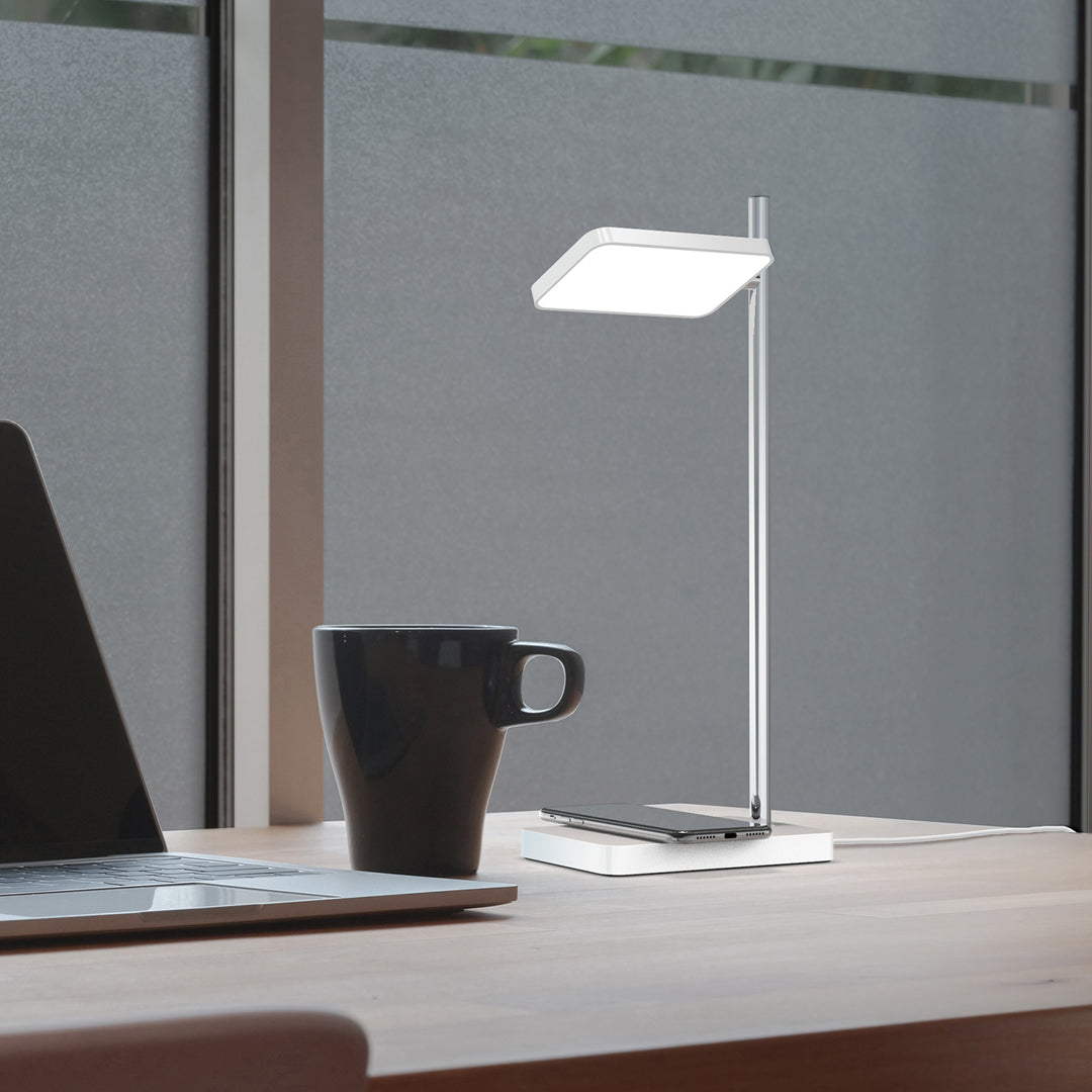 Sleek silver desk lamp with a modern white shade, set against a warm wood desk and dark coffee cup.