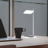 Sleek silver desk lamp with a modern white shade, set against a warm wood desk and dark coffee cup.