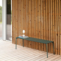 Green metal bench with a smooth finish, paired against a warm, striped wooden wall.