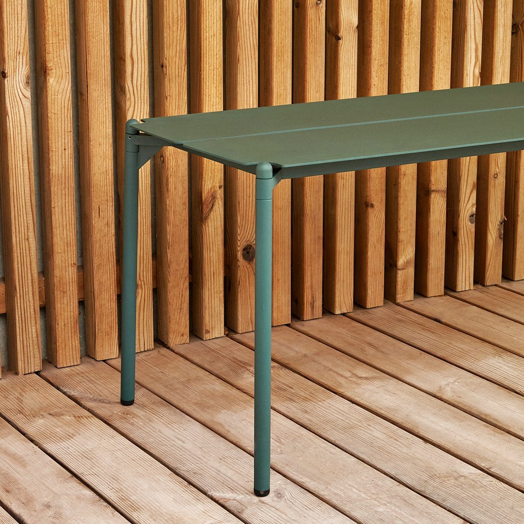 Green slatted table with sleek metal legs, set against a wooden backdrop for a natural, modern feel.