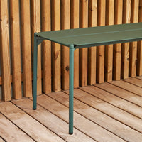 Green slatted table with sleek metal legs, set against a wooden backdrop for a natural, modern feel.