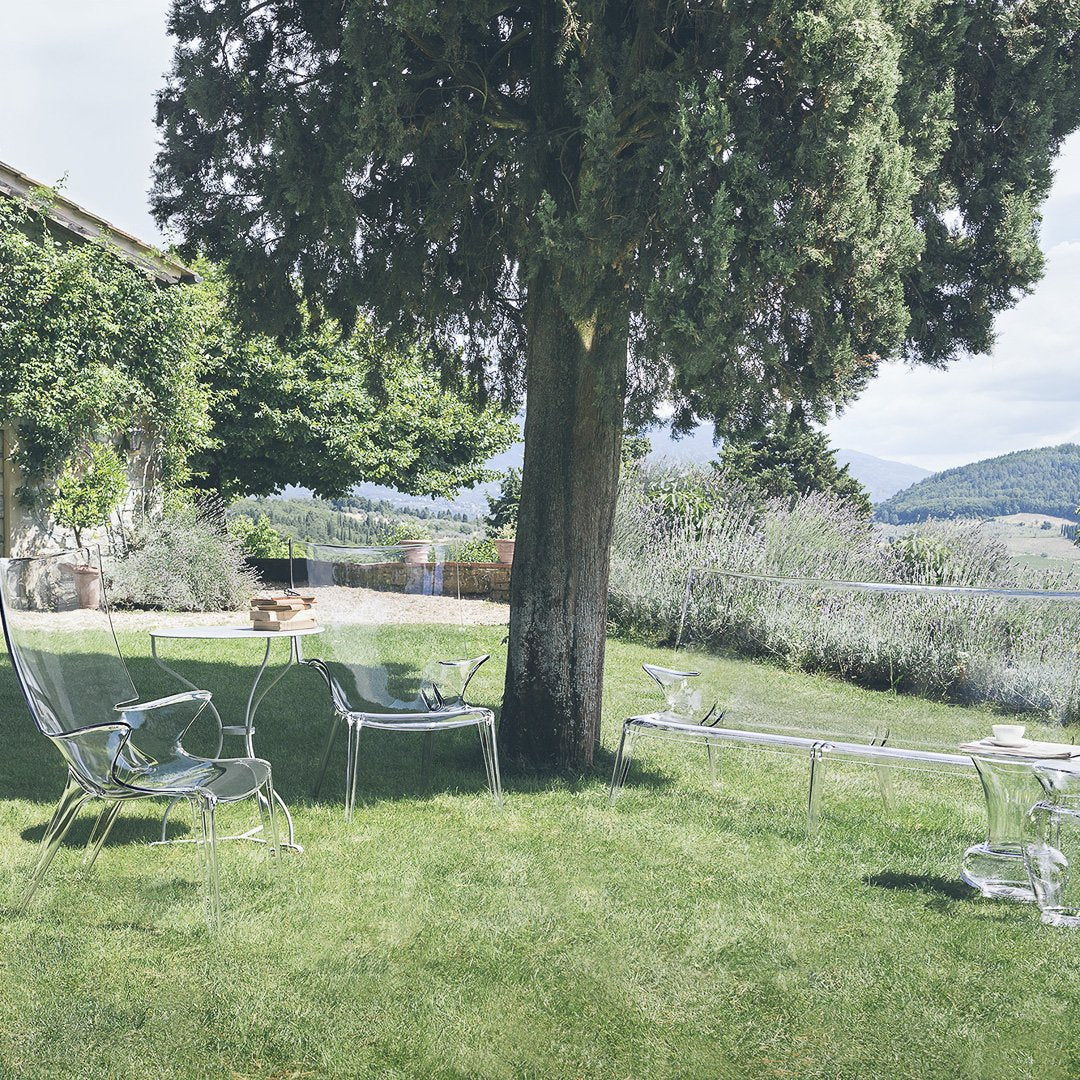 Translucent acrylic outdoor furniture in clear and green hues, set against a lush garden backdrop.
