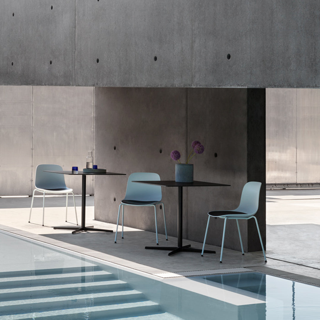 Light blue chairs and a dark table against a textured gray wall, featuring a minimalist design by a pool.