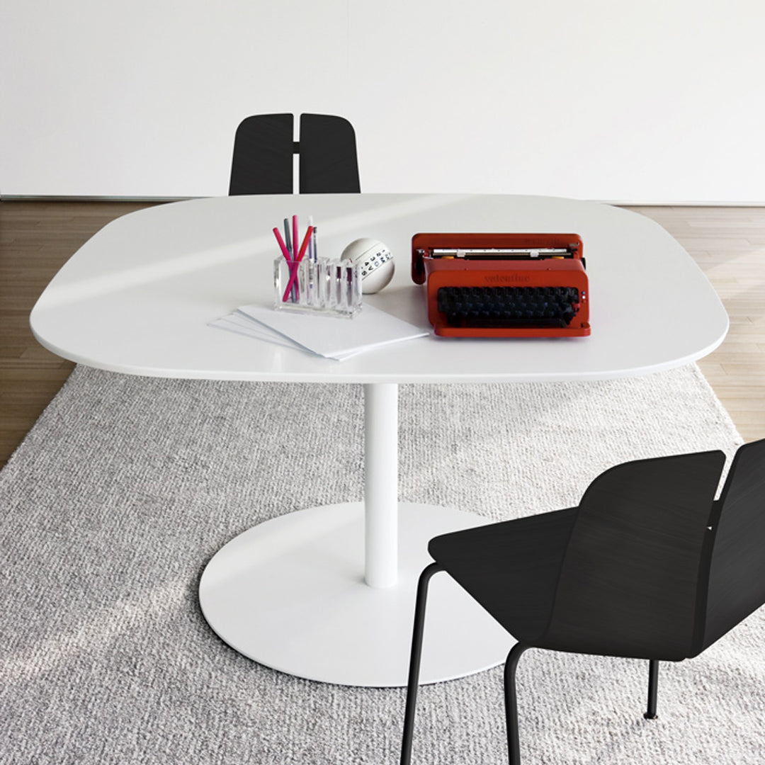 White oval table with a smooth surface, accompanied by black chairs and a light gray rug.