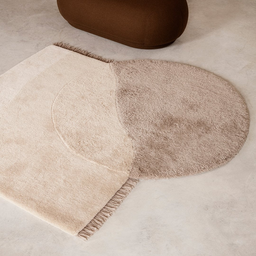 Cream and beige circular rug with soft fringe detailing and a smooth texture, adding warmth to any space.