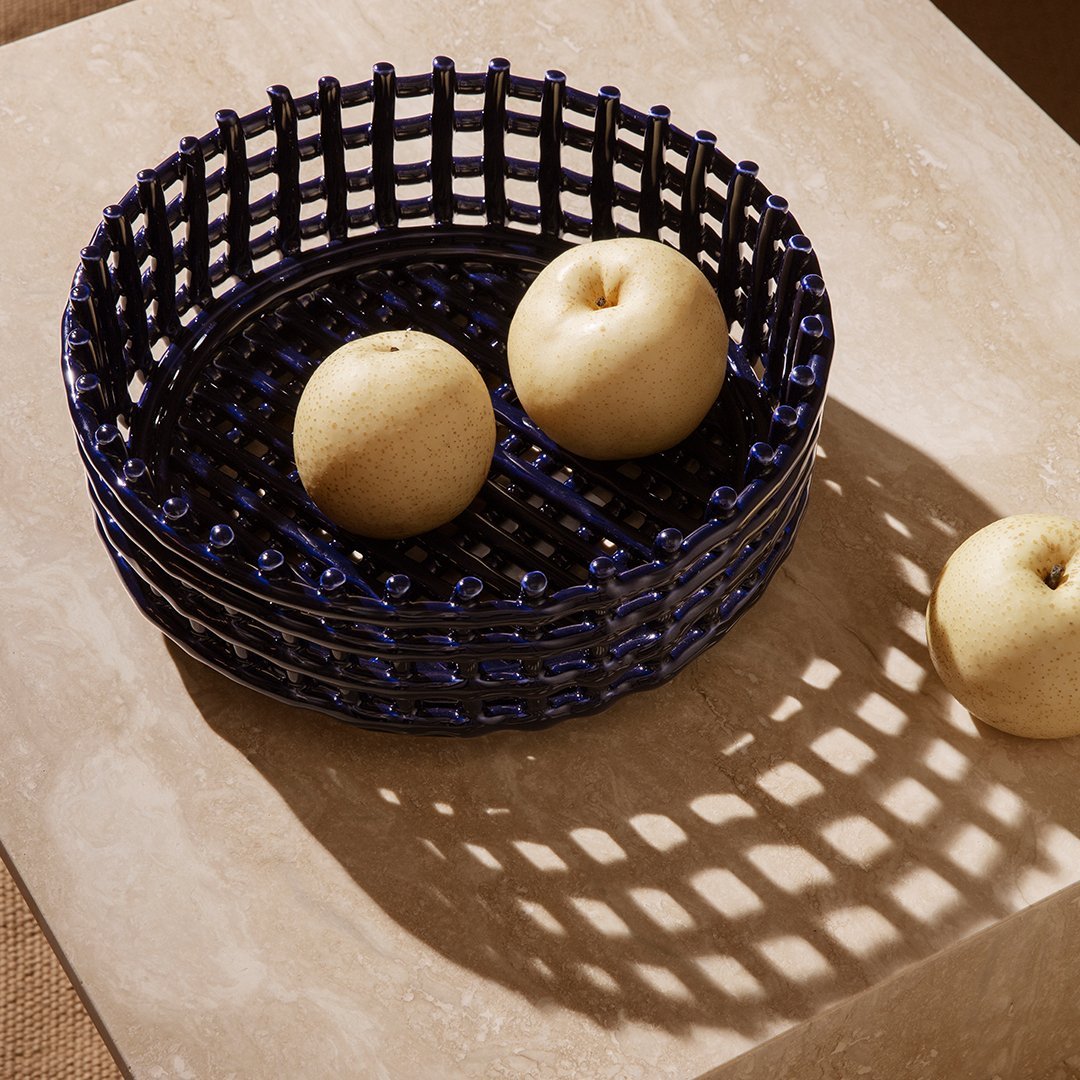 Navy blue woven basket with a geometric pattern, featuring two pale yellow apples on a beige countertop.